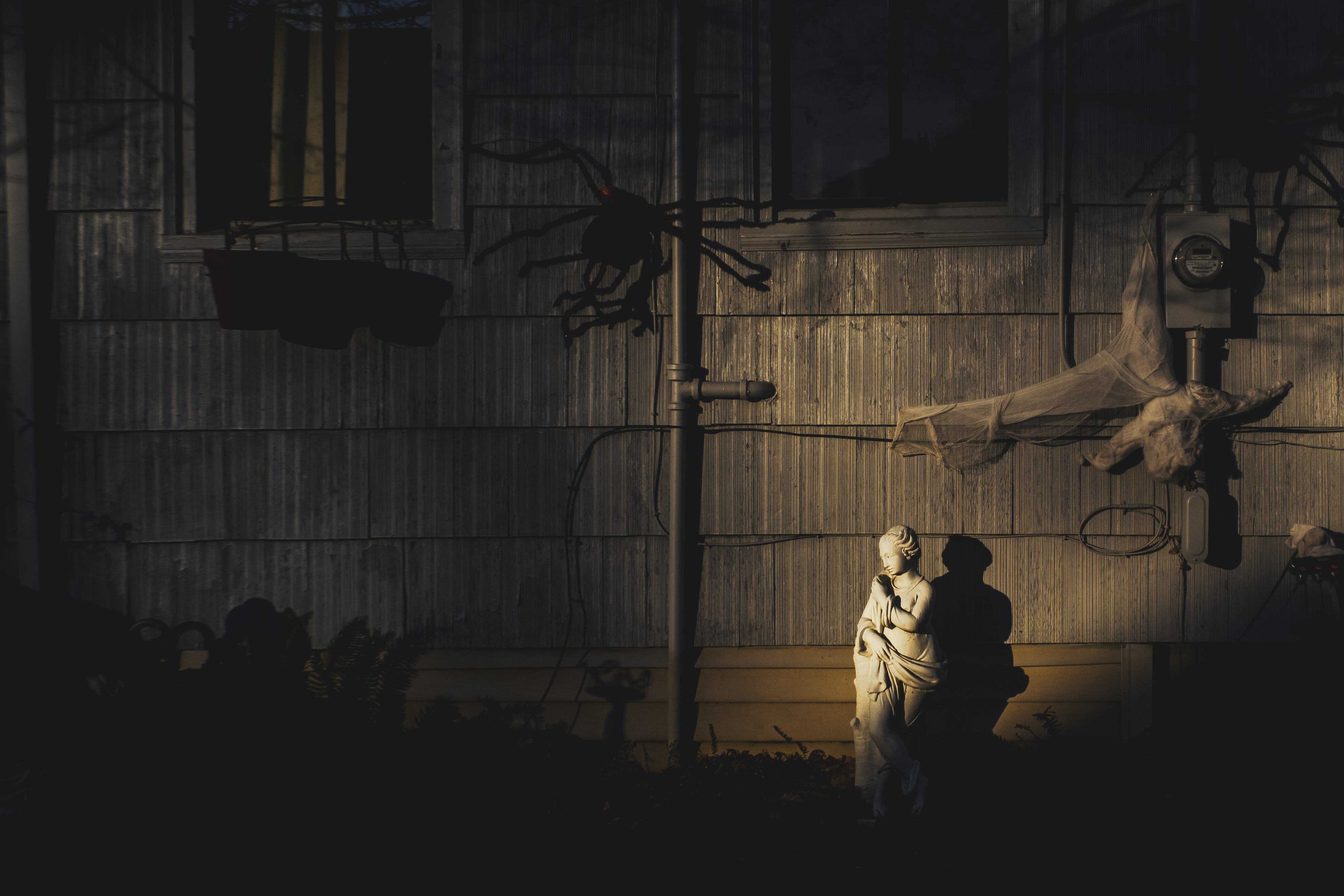 A pseudo-classical yard statue in the shadow of a gray house. Strong shadows.