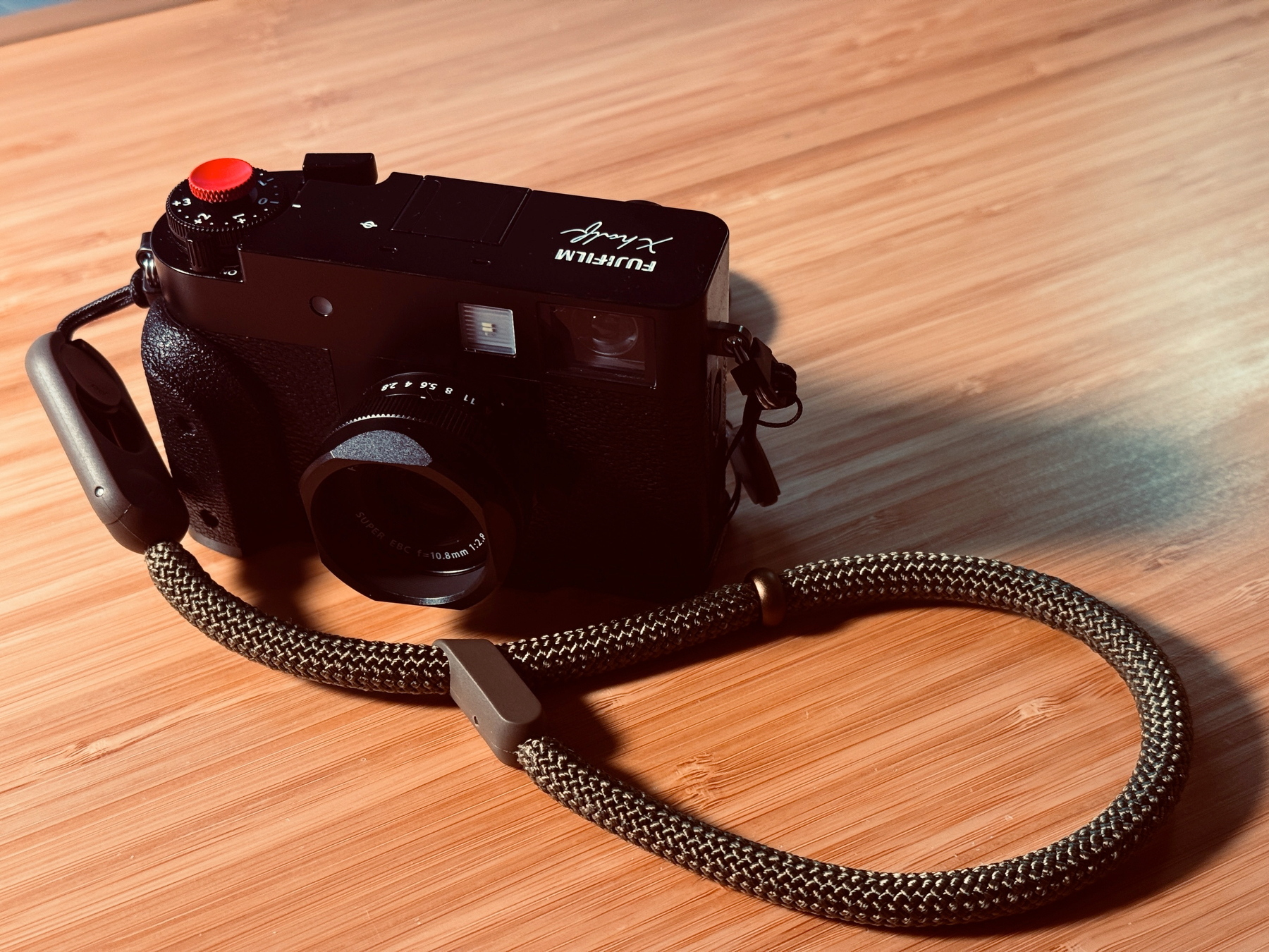 A Fujifilm X half with  a rope wrist strap  on a wooden surface.