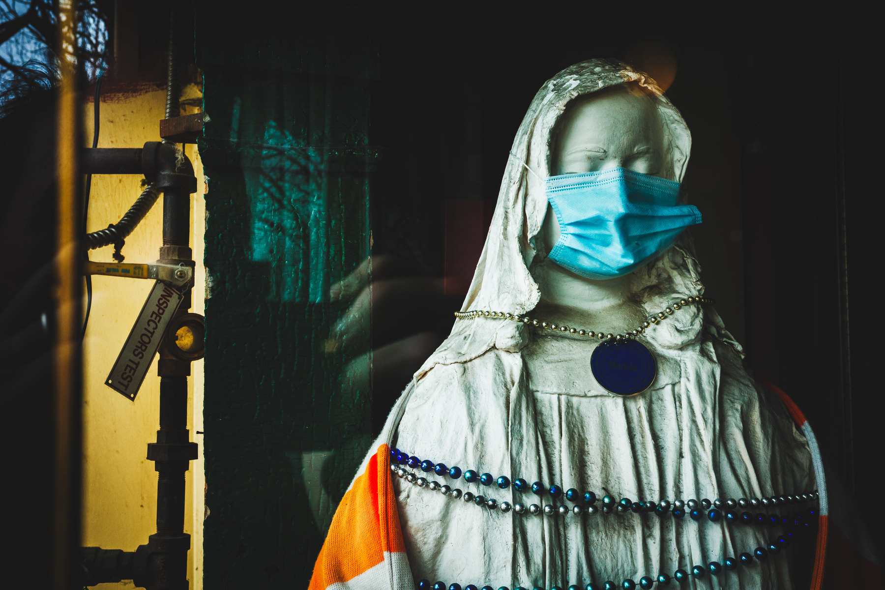 A statue of a robed figure is adorned with a beaded necklace and a blue mask against a dark background.
