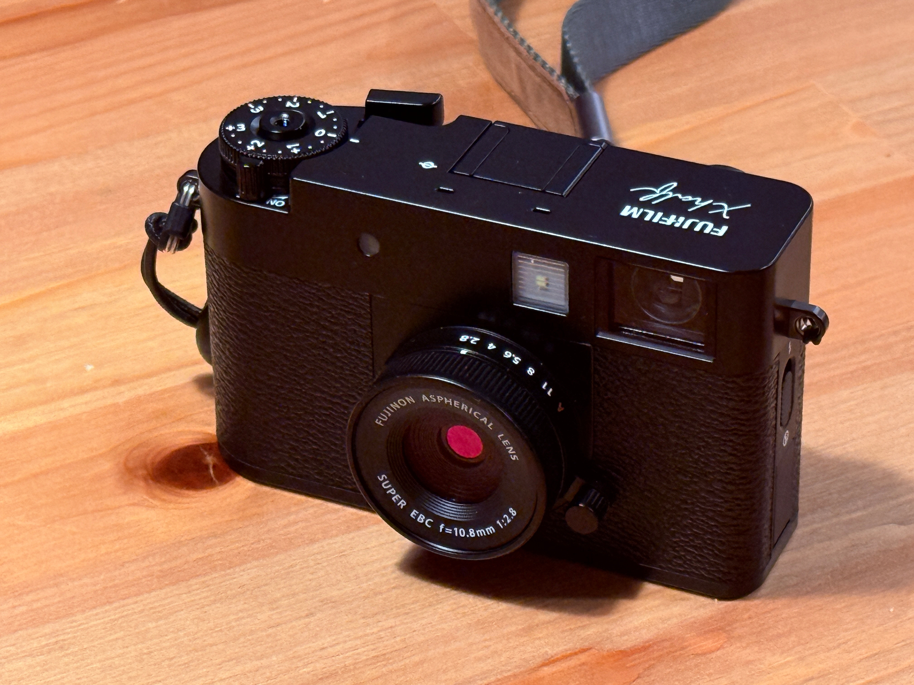 A Fujifilm X half camera is resting on a wooden surface.