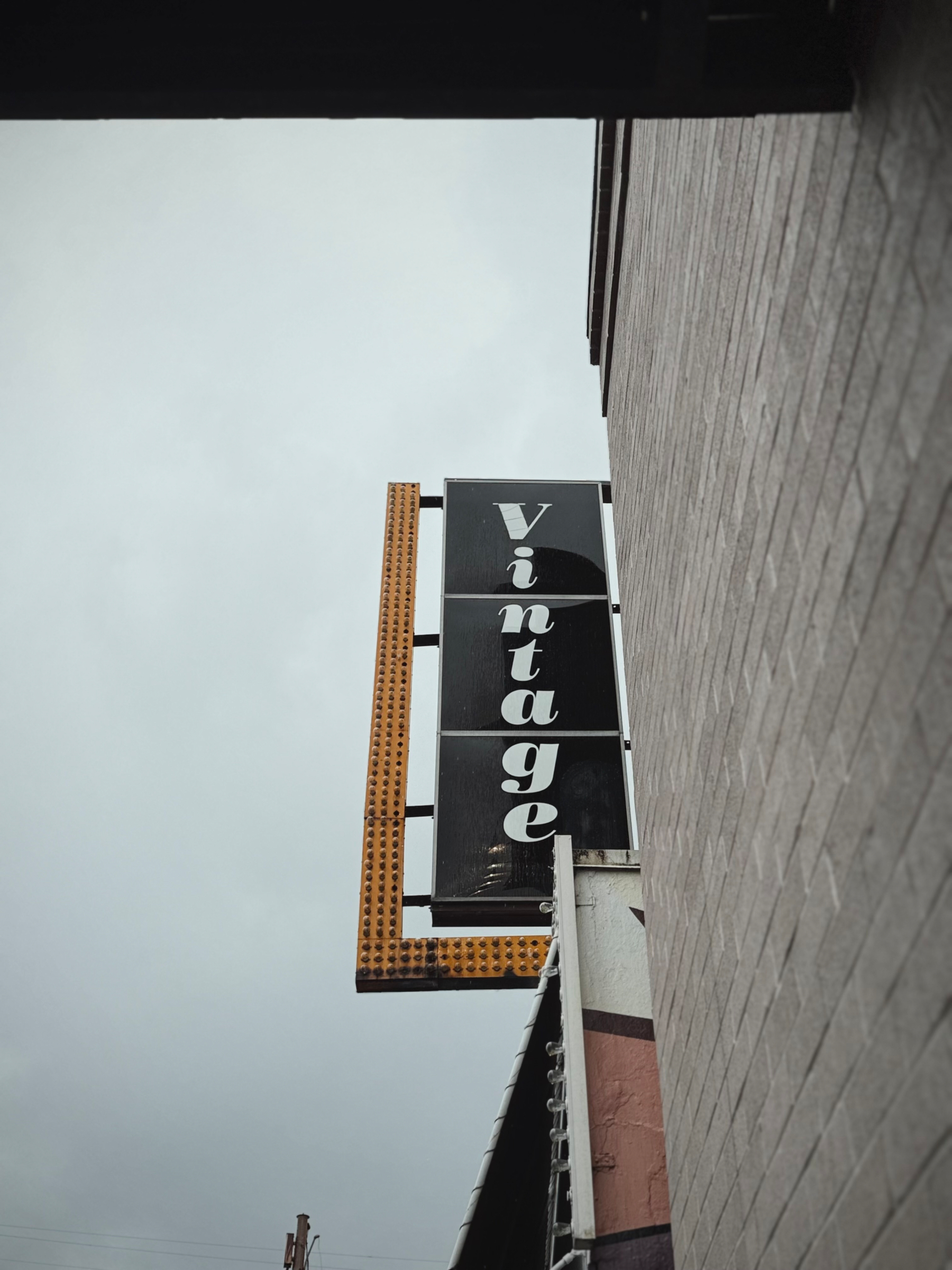 A vertical sign attached to a building displays the word vintage against a cloudy sky background.